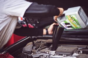 Person pouring synthetic motor oil into a clean engine bay of a modern vehicle indoors.