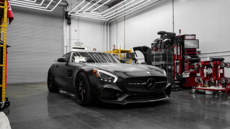 A technician checks under the hood of a luxury sedan inside a well-lit auto repair shop.