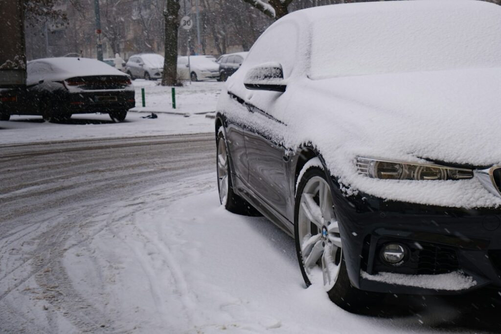 Luxury sedan parked outdoors on a cold morning with frost on the windshield and a person checking tire pressure.