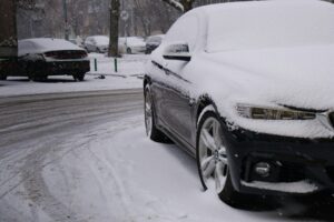 Luxury sedan parked outdoors on a cold morning with frost on the windshield and a person checking tire pressure.