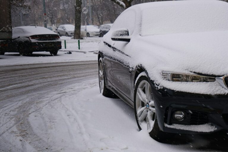 Luxury sedan parked outdoors on a cold morning with frost on the windshield and a person checking tire pressure.