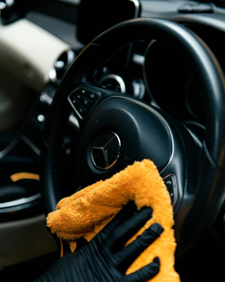 A person gently dries a polished luxury sedan with a clean microfiber towel in a shaded driveway. KEYWORDS: ["luxury car paint protection", "hand washing luxury vehicle", "microfiber towel car detailing"]