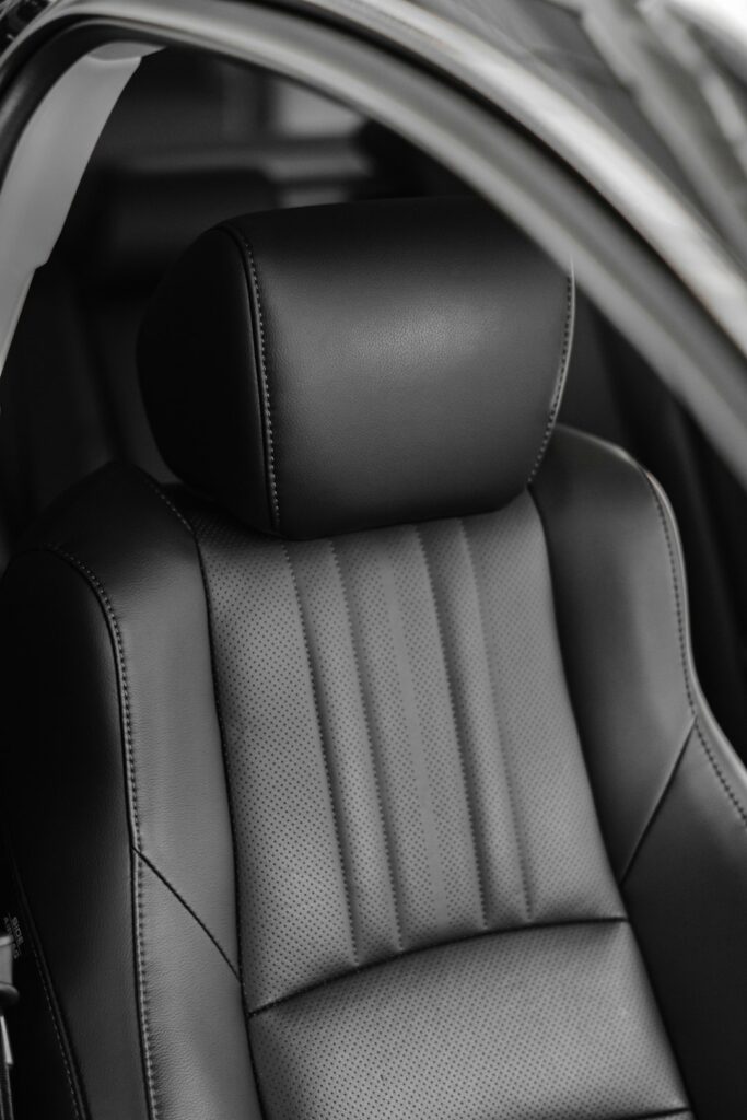 A person gently cleans perforated leather car seats with a microfiber cloth inside a luxury vehicle.