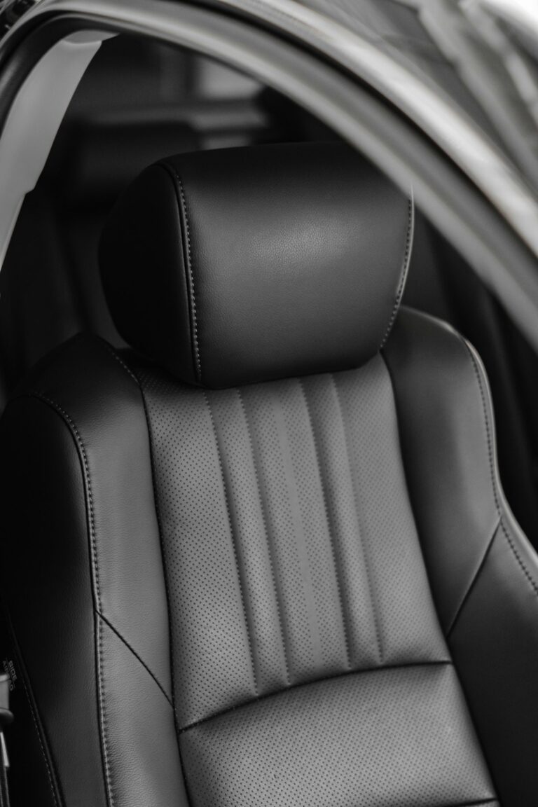 A person gently cleans perforated leather car seats with a microfiber cloth inside a luxury vehicle.